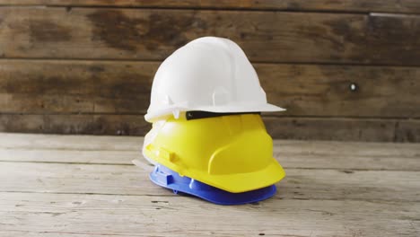 Video-of-close-up-of-colourful-building-helmets-on-wooden-background