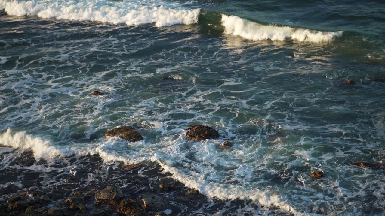 Primo piano di onde oceaniche spumeggianti che si infrangono su una spiaggia rocciosa, 4K.