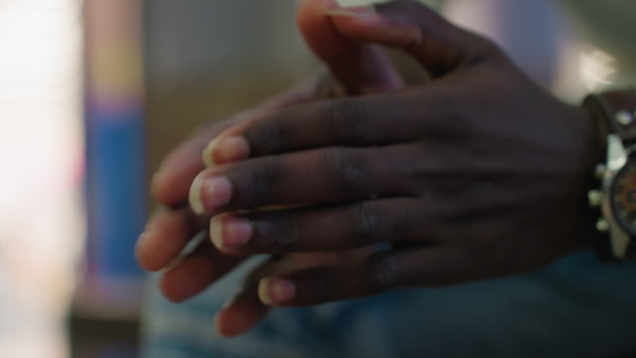 Close up of dark skin person tapping hands together wearing wristwatch detailed view of fingers and gesture indoors with soft blurred background lifestyle moment focus on expression