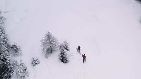 Couple-walks-across-a-snowy-field-in-snowshoes,-as-the-drone-pans-around-them-and-flies-up