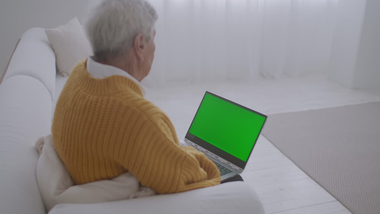 una mujer mayor mira un monitor con una pantalla verde y habla a través de un enlace de video con su nieta o hija o un médico. ayuda de video para los ancianos. la abuela usa una computadora portátil