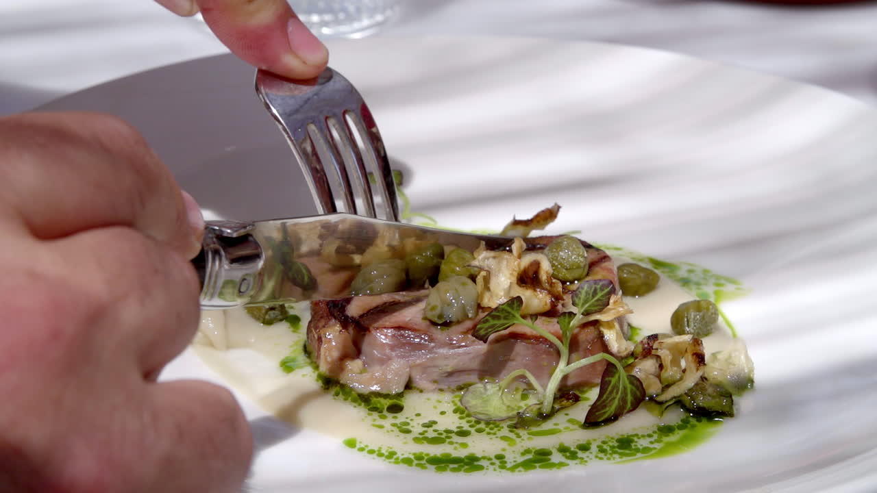 Person cutting a gourmet dish with a knife and fork