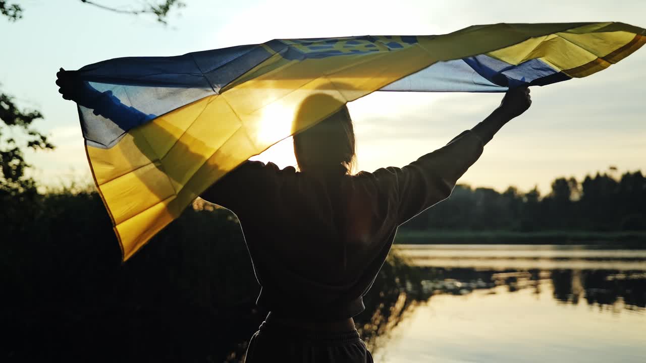 Silueta de mujer izando la bandera ucraniana al atardecer simbolizando la libertad