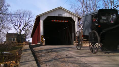 an amish horse cart travels through a covered bridge along a road in rural pennsylvania 2
