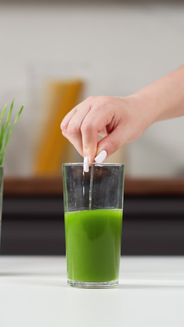 손 을 가진 손 이 초록색 밀 풀 주스 의 높은 잔 에  을 입 하고 있다