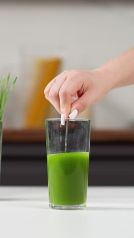 mano con uñas blancas insertando una paja en un vaso alto de jugo de pasto de trigo verde