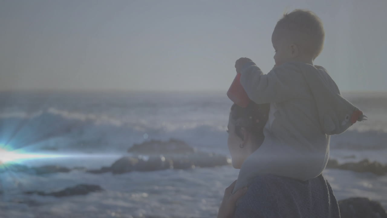 Walking on beach, mother carrying child on shoulders, both enjoying animation