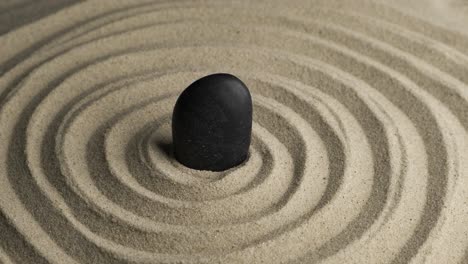 rotation of the black stone in the center of the sand spiral. close-up of patterns in the sand