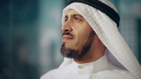 portrait of successful muslim businessman in traditional outfit gently smiling, wearing white kandura and black agal keeping a ghutra in place. saudi, emirati, arab businessman concept.