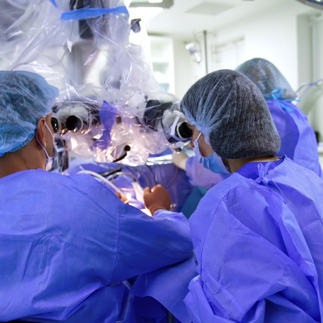 Rear view of surgeon sitting at the microscope. Neurosurgical operation on brain in modern hospital.