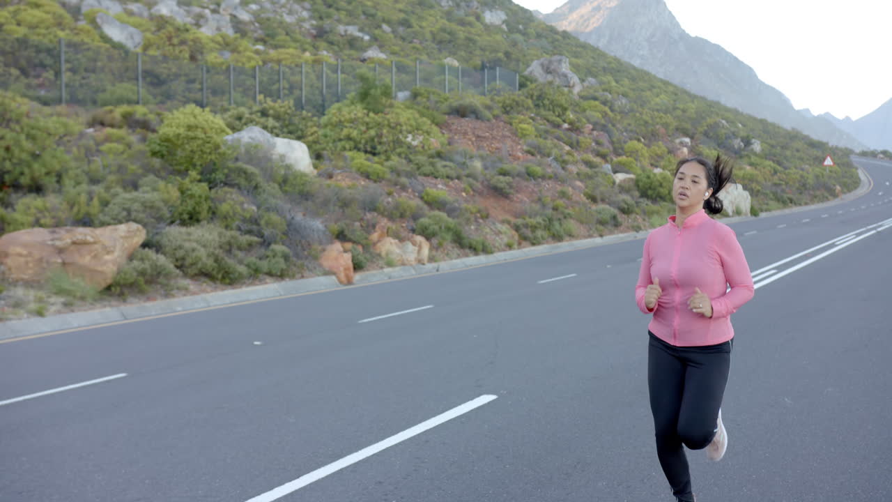 Donna che fa jogging su strada di montagna, con giacca rosa, si gode l'esercizio all'aperto, spazio per la copia.