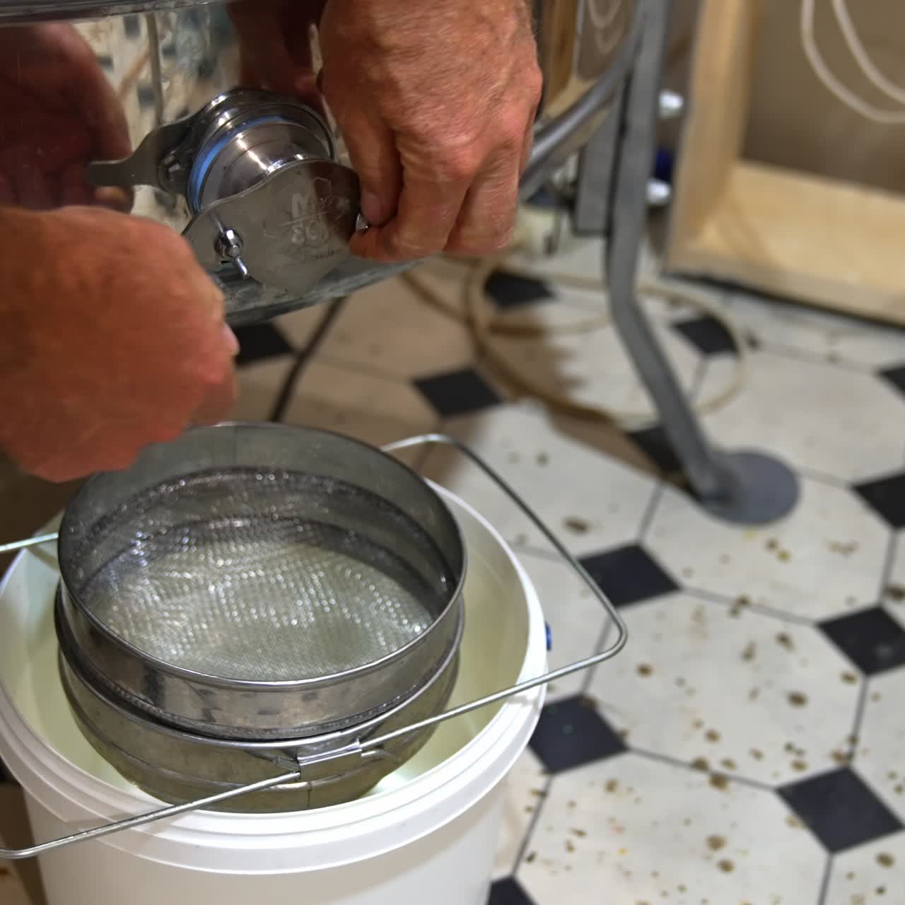 Man opens the faucet at honey extracting machine. Fresh golden organic liquid honey flows into the bucket standing under the equipment