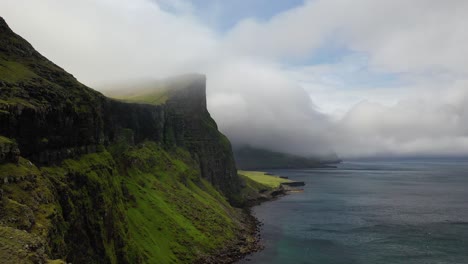 Persona-En-La-Cima-Del-Acantilado-De-Las-Islas-Feroe-Con-Fondo-De-Nubes-Marinas,-Revelación-De-Sobrevuelo-Aéreo