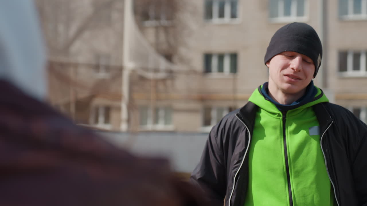 Un atleta concentrado escucha atentamente a su mentor; un atleta adolescente interactúa con su entrenador en un entorno deportivo urbano; un joven deportista recibe orientación atentamente en un campo de juego urbano.