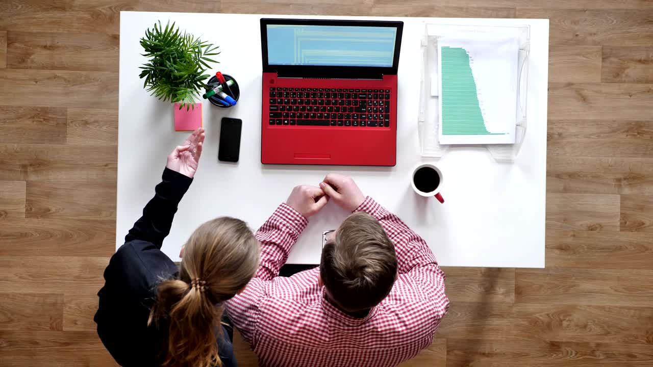 joven con gafas hablando con mujeres a través de la computadora portátil, topshot, sentado detrás del escritorio con café y documentos