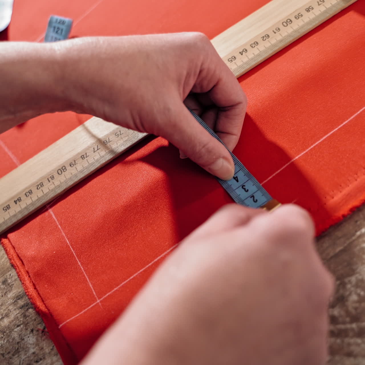 Female's hands are sketching lines with a tape measure and a soap on a table. Sewer works with red fabric and a ruler in atelier. Handicraft concept.