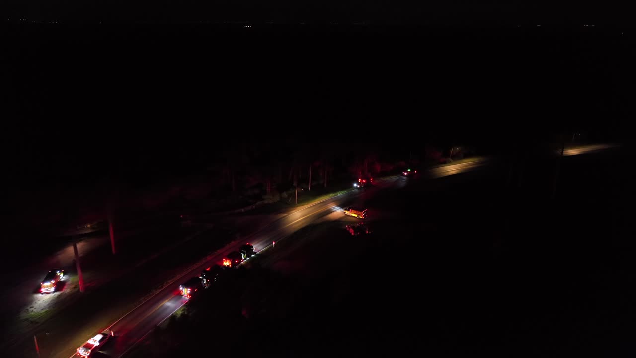 Flashing red lights of medical cars at night. Aerial flyover shot. Highway intersection with fire trucks and ambulance vehicles during fire operation. American city suburb in Florida, United States.