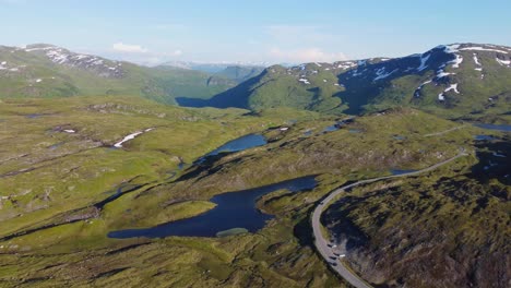 Carretera-De-Montaña-Con-Curvas-Con-Coches-Que-Pasan-En-La-Cima-De-La-Montaña-Vikafjell-Noruega---Vista-Aérea-De-La-Puesta-De-Sol-De-Verano-Por-La-Noche-Con-El-Valle-De-Myrkdalen-En-Segundo-Plano