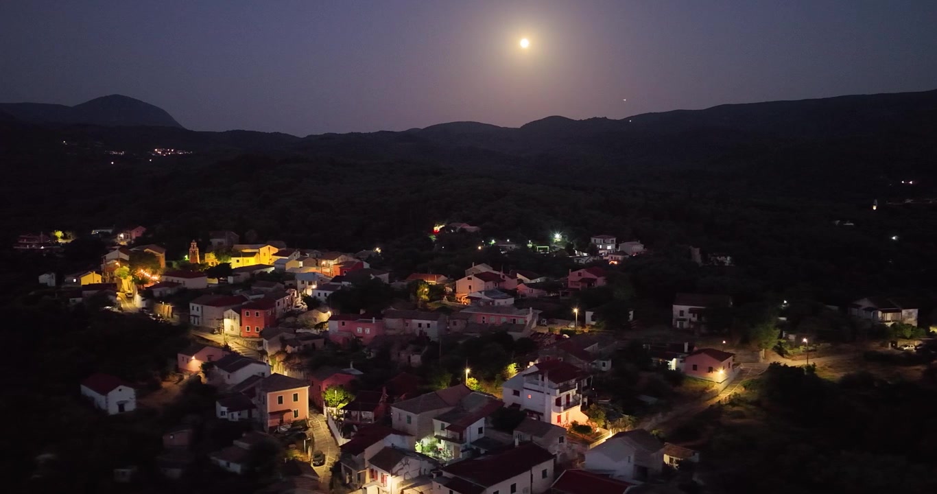 Vista aérea noturna da tradicional vila de Agioi Douloi iluminada sob a lua cheia em Corfu, Grécia.