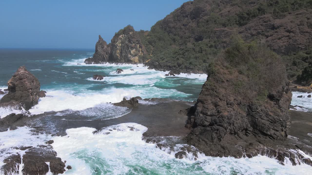 Powerful ocean waves hitting rocky coast of Indonesia, aerial orbit view