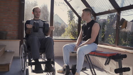 disabled man in wheelchair working out with dumbbell at home while his personal trainer assisting him