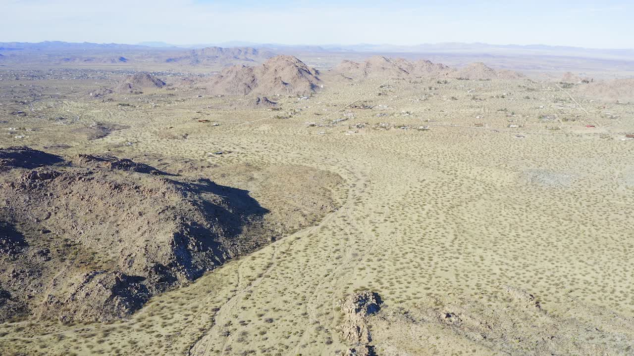 Aerial view of Joshua Tree national park wilderness and dry land with slow tilt up to Horizon.