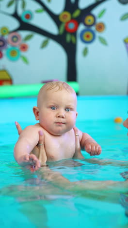 female hands hold a cute little baby in the swimming pool. lovely kid is learning to swim. vertical video.