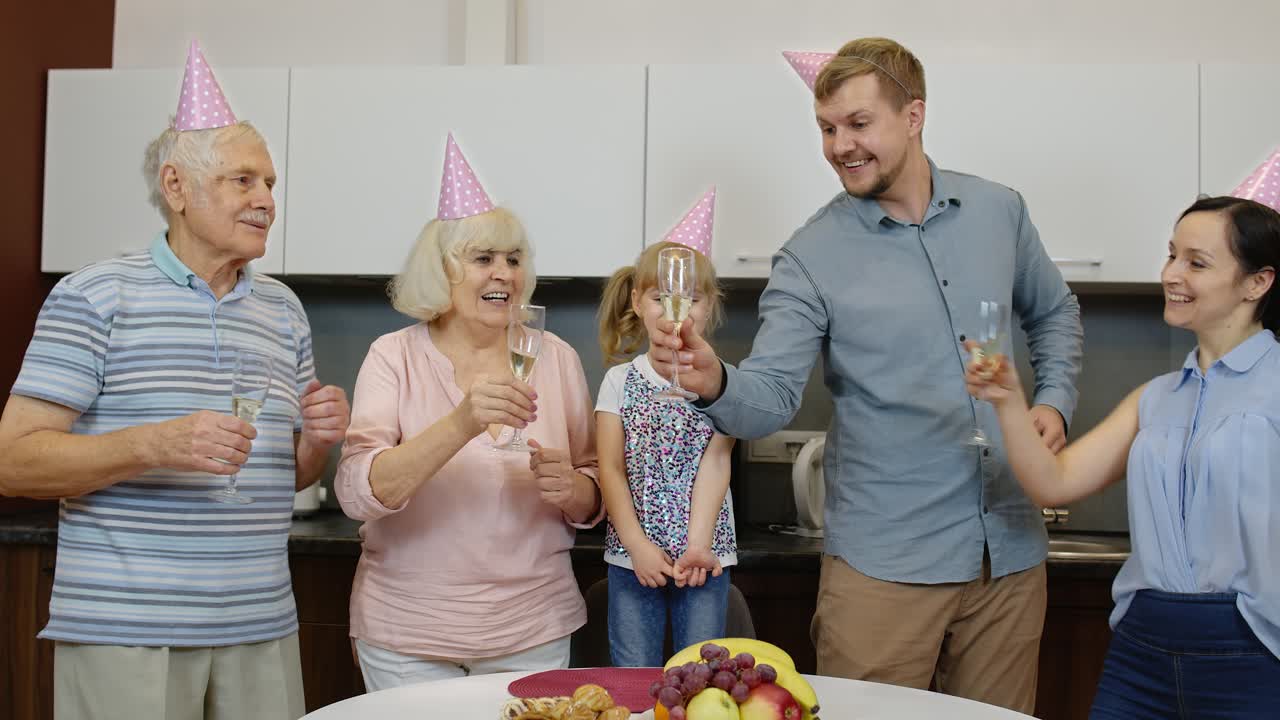Membri della famiglia multigenerazionale con una bambina che festeggiano una festa di compleanno. Bevono champagne.