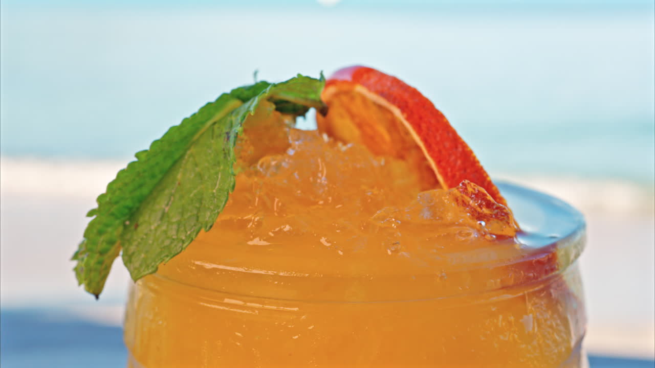 Close up of an orange cocktail on a table with a blurred view of the sea on the background