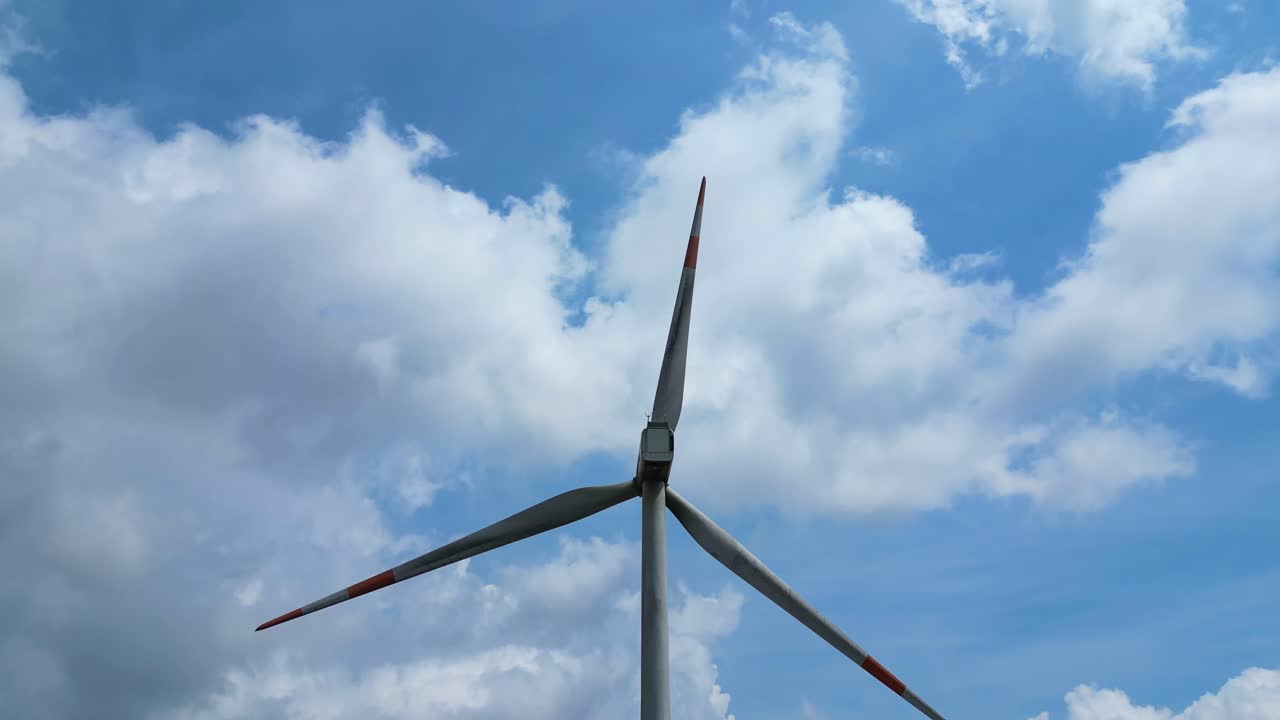Large wind turbine turning against blue cloudy sky, global renewable energy symbol