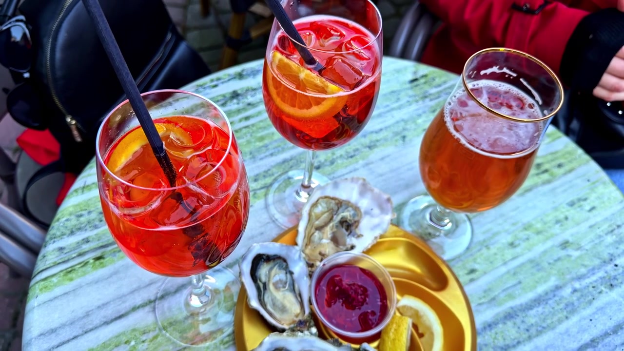 Aperol spritz cocktails, beer and fresh oysters served on a café table, creating a colorful outdoor dining and seafood aperitif scene.