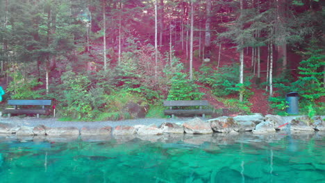 Low-sideways-drone-shot-of-older-sporty-woman-running-by-a-beautiful-lake-in-nature