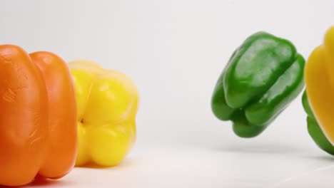 colorful medley of red, orange, yellow and green bell peppers falling onto white table top and bouncing off each other in slow motion