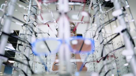 eyeglasses shop. stand with glasses in the store of optics. beautiful woman choosing glasses at optical store