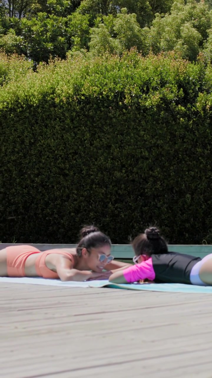 Vertical video: Lying mom and kid in swimwear touching leaning on pool deck pointing at towel item