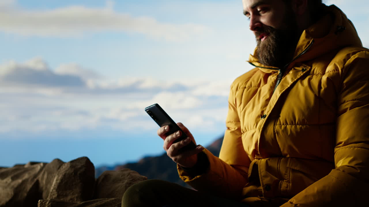 viajero sentado y navegando su teléfono en la cima de la montaña rocosa
