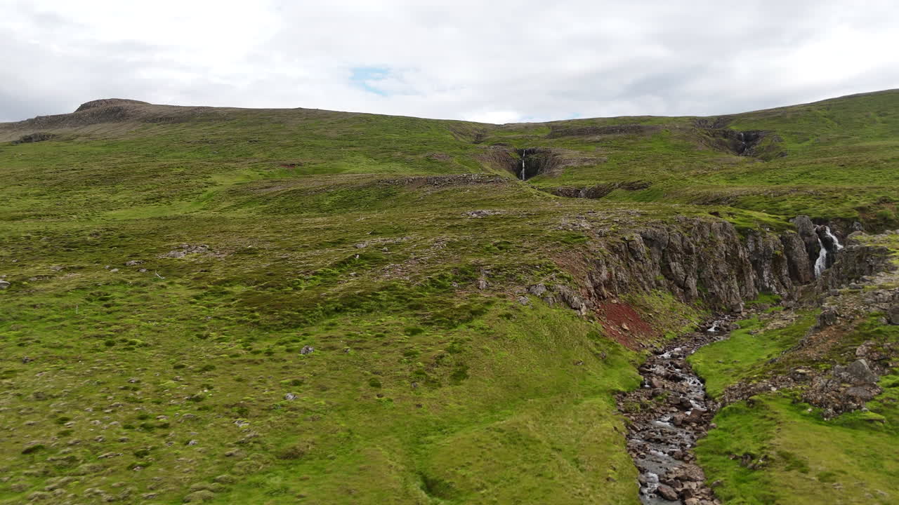 Wide aerial view of open grasslands and long mountain slopes along Road 59 in Dalabyggð, showing farmland patterns, rural terrain, and soft overcast light across the valley