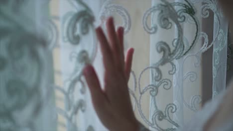 la mano tocando una cortina de encaje en una ventana