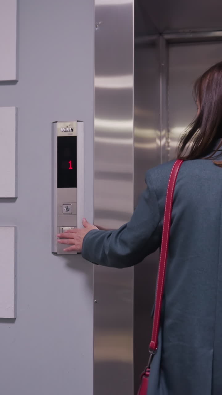 Businesswoman walking down modern office hallway toward elevator with briefcase, wearing formal attire in professional setting. Corporate environment, career, business concepts