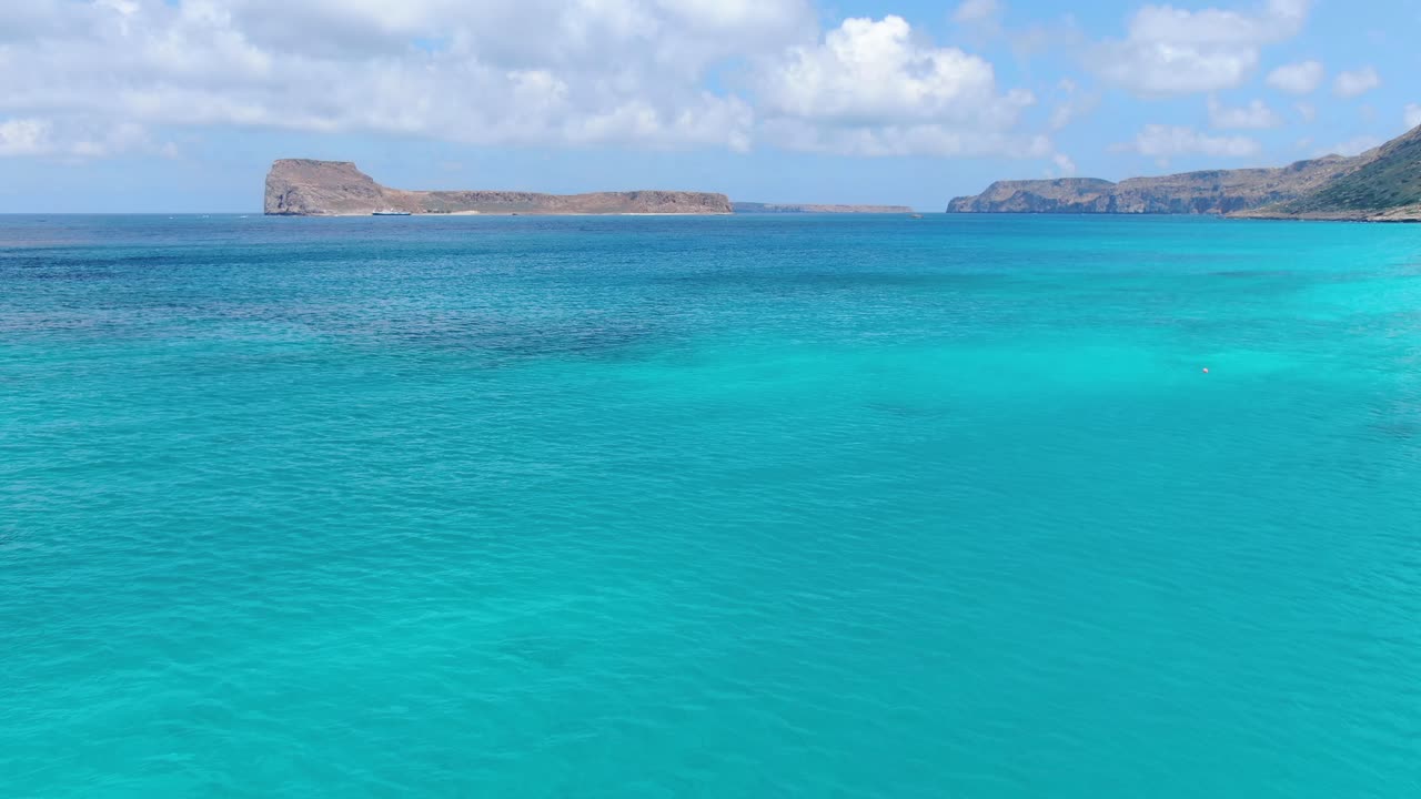 Approaching Gramvousa beach near Balos Beach in Crete Greece with blue turquoise-colored water and rocky isles, Aerial flyover shot