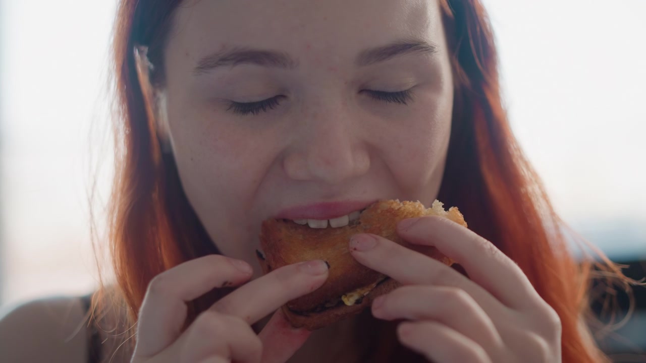 Mujer joven sosteniendo un pastel cerca de la boca, un primer plano íntimo de degustación captura movimientos cuidadosos de las manos y la textura crujiente, masticación sutil, luz de estudio con un suave desenfoque de fondo, expresiones pensativas.
