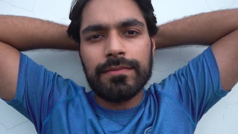 casual man poses with hands behind his head while smiling at the camera on white wall background - medium close up