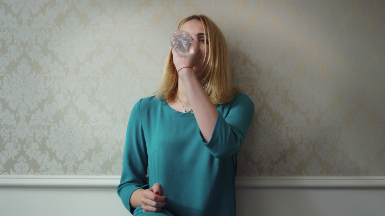 Giovane donna che apre bottiglia di plastica e acqua potabile sulla parete chiara del fondo