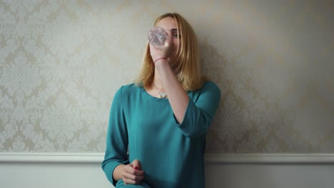 Young-woman-opening-plastic-bottle-and-drinking-water-on-background-light-wall