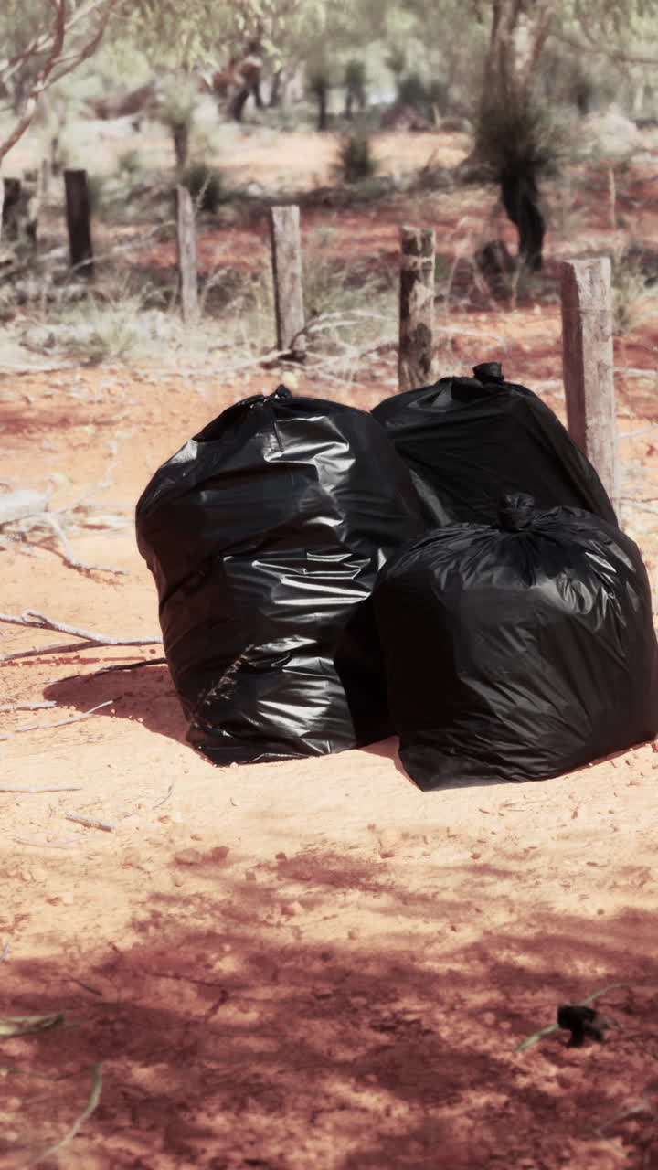 세 개의 검은색 쓰레기 봉투가 사막의 길에 앉아 있습니다.
