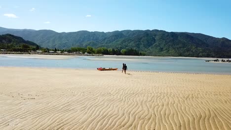 slowmotion aerial view on two people approaching kayak in beach lagoon on sandy bay, new zealand