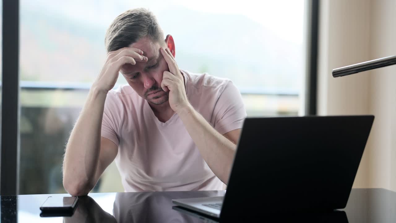 Pensive sad businessman looking at computer screen sitting at table at home