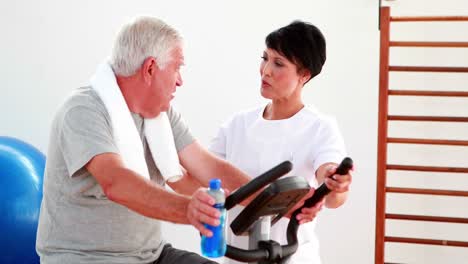 Elderly-man-using-the-exercise-bike-talking-to-physiotherapist