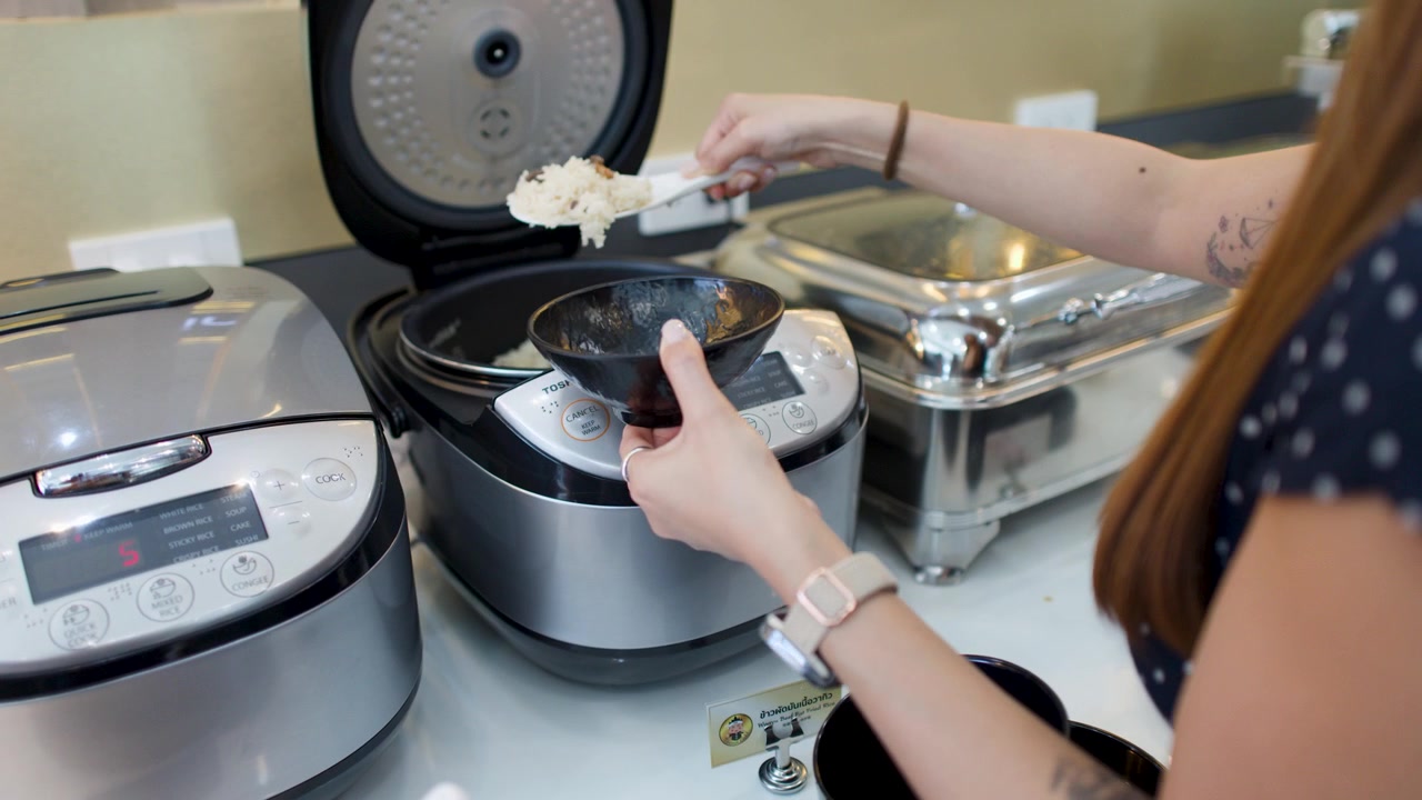 A woman in a polka dot shirt scoops rice into a bowl at a buffet