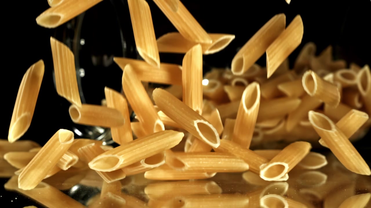 Pasta penne cruda che cade al rallentatore su sfondo nero